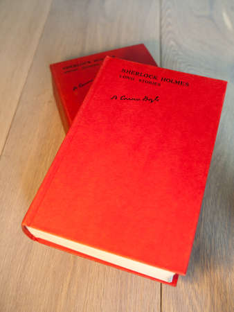 Aged copies of sherlock holmes long and short stories standing on a wooden table with a book shelf full of books in soft focus behindのeditorial素材