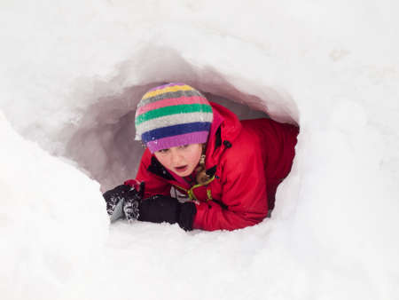 small girl in winter clothes playing in a snow holeの写真素材