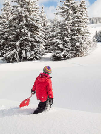 small girl walking in deep snow with sledge in hand and wooded winter  mountain landscape behindの写真素材