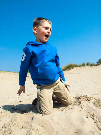 small boy playing in sand at the base of a sand dune on a bright sunny spring dayの写真素材
