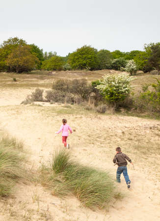 small boy and girl running away from camera into a dune landscape in springの写真素材