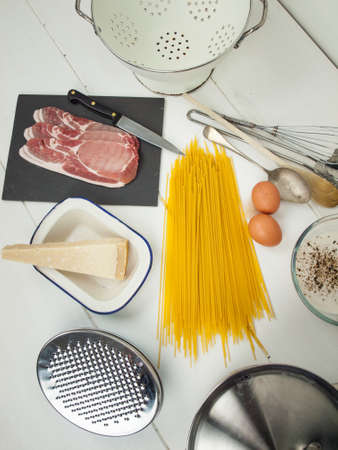 ingredients for spaghetti carbonara with pots, pans and utensils on a rustic white kitchen surfaceの写真素材
