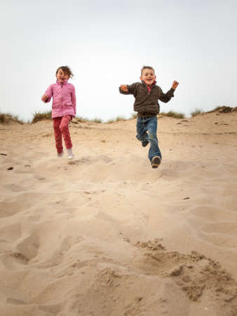 small boy and girl running towards cameradown a sand dune landscape in springの写真素材