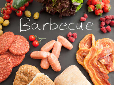 raw barbecue meat with fresh fruit, vegetables and bread on a blackboard carrying the word barbecueの写真素材