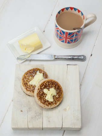 English crumpets with butter on a rustic white table top with a cup of english tea in a union jack mugの写真素材