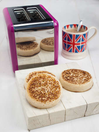 English crumpets on a rustic white table top with a toaster and a cup of english tea in a union jack mug behindの写真素材