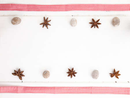 rows of star anise and nutmeg with checked red ribbon on a rustic, aged, white wooden table topの写真素材