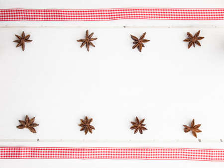 rows of star anise  with checked red ribbon on a rustic, aged, white wooden table topの写真素材