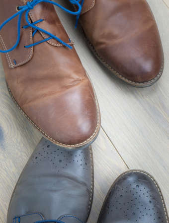 detail of two pairs of grey and brown  leather shoes toe to toe against an aged oak floor. stepping on toe conceptの写真素材