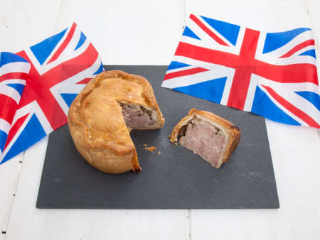 sliced english pork pie on a black slate with rustic white table top behind and union jack flagsの写真素材