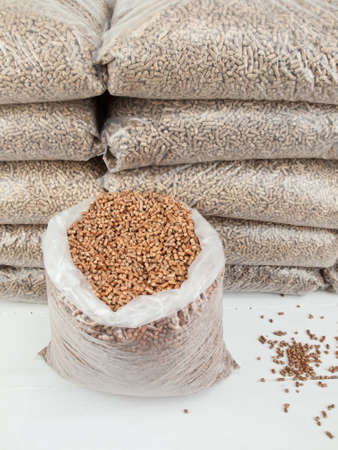 An open bag of wood pellets with a stack of bagged wood pellets in storage behindの写真素材