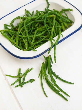 close up of fresh green marsh samphire in a white enamel dish on a rustic white wooden table topの写真素材