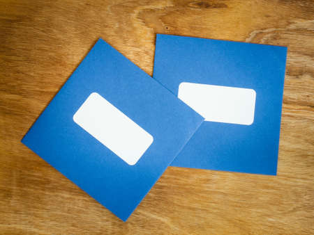 two plain blue square envelopes with blank window against an aged grained wooden backgroundの写真素材