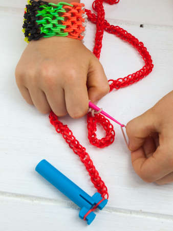 childs hands making a colourful elastic loom band bracelet against a white table topの写真素材