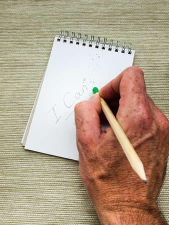 man hand erasing the letter T from the word can't written in pencil on a spiral bound note pad using a pencil top eraserの写真素材