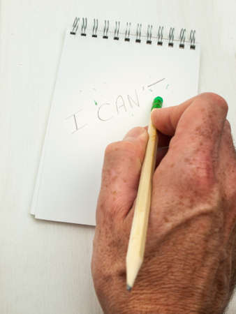 man hand erasing the letter T from the word can't written in pencil on a spiral bound note pad using a pencil top eraserの写真素材