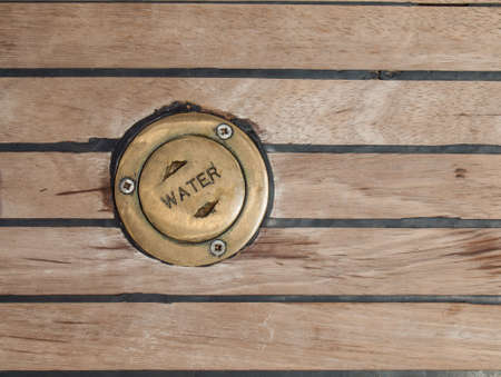 bronze cap carying the word water in a ships teak deck