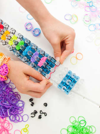 childs hands placing colourful elastic loom bands on a band loom against a white table topの写真素材