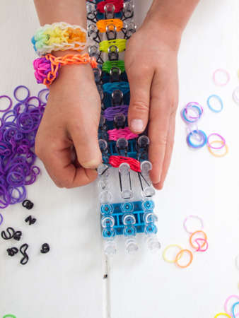 childs hands making a braclet with colourful elastic bands on a band loom against a white table topの写真素材