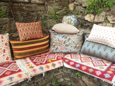 arrangment of cusions and a turkish kelim on a stone corner bench against a rustic stone garden wallの写真素材