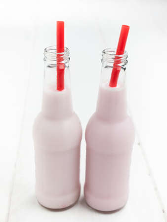 two bottles of pink milk with red straws on a white wooden table topの写真素材