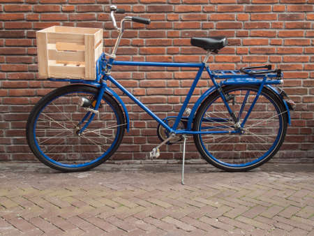 traditional blue cargo bike with wooden crate against a red brick wallの写真素材