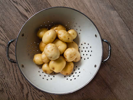 washed new potatoes  in a retro white enamel collander against a wooden backgroundの写真素材