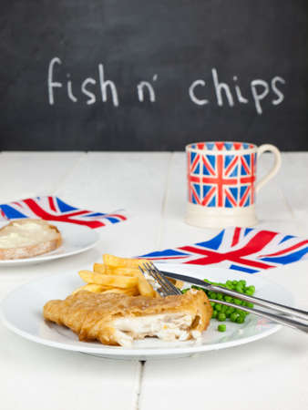 a meal of  english fish chips and peas, a slice of bread and butter, a mug of tea in a union jack...