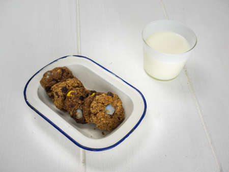 rustic home baked cookies in an old enamel bowl with a glass of milk on a rough white table topの写真素材