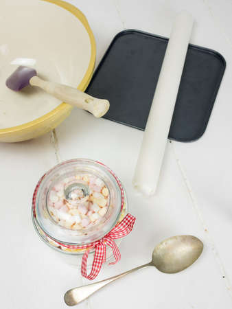 cookie ingredients in an open glass jar with kitchen utensils on a rustic white table topの写真素材