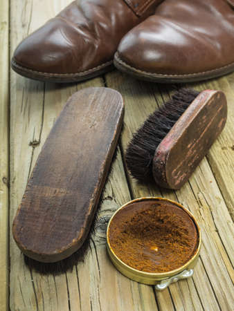 closeup of shoe polish and antique brushes against  aged cracked  wooden boards with old brown leather shoes behindの写真素材