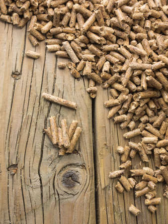 overhead view of extruded woodpellets on old cracked knotted wooden boards with wood pellets in soft focus behindの写真素材