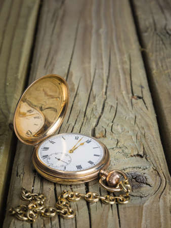 antique golden pocket watch with fob chain against rustic aged wooden background with hands approaching twelve o'clockの写真素材