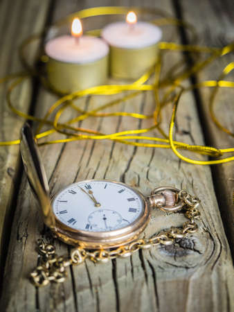 antique golden pocket watch with fob chain against rustic aged wooden background with hands approaching twelve o'clockの写真素材
