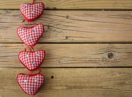 line of of four red check hearts  with red ribbon on rustic wooden background