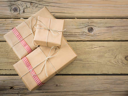 three brown paper parcels with red check ribbon against an aged wooden backgroundの写真素材