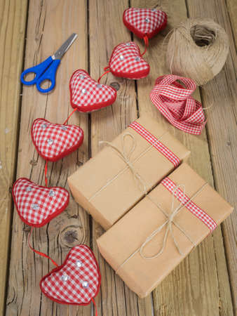 three parcels wrapped with brown paper and string with ball of string red check ribbon and scissors against an aged wooden backgroundの写真素材