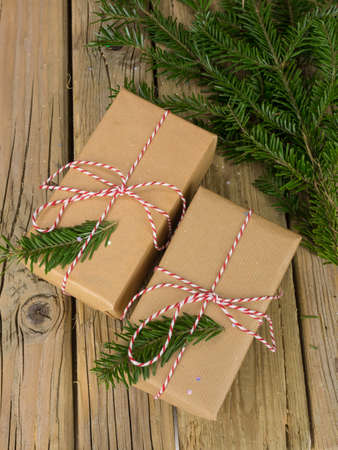 overhead view of parcels wrapped in  brown paper with red and white string against an aged wooden background with conifer branchesの写真素材