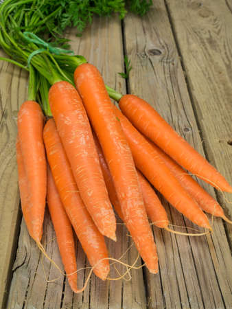 bunch of fresh carrots with green leaves against aged wooden backgroundの写真素材