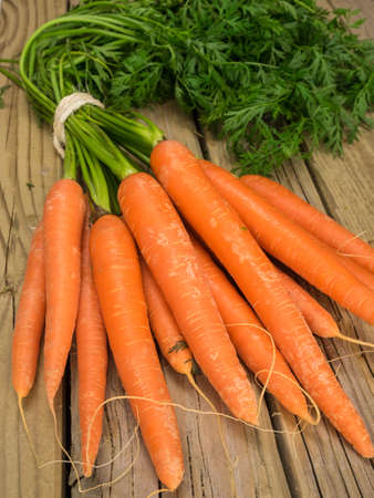 bunch of fresh orange carrots with green leaves against aged wooden backgroundの写真素材