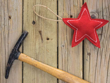 red and white  fabric christmas star  with tack hammer and  iron nail against a background of rustic wooden boardsの写真素材