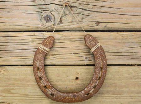 closeup of rusty iron horseshoe hung on a nail in an aged knotted wooden wall with horseshoe centeredの写真素材
