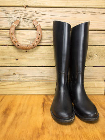 dirty riding boots against a stable wall with horseshoe