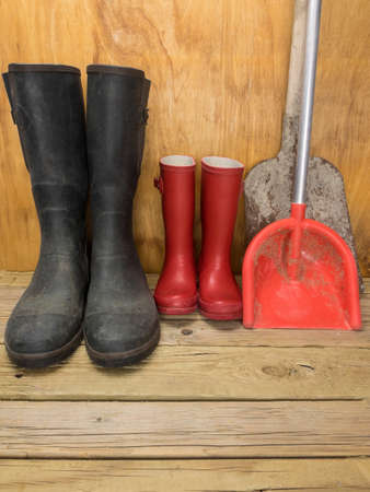 mans green rubber boots and childs red rubber boots in a shed with tools father and son conceptの写真素材