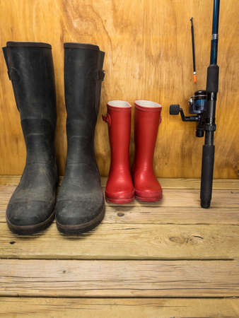 mans green rubber boots and childs red rubber boots in a shed with fishing rod father and son conceptの写真素材
