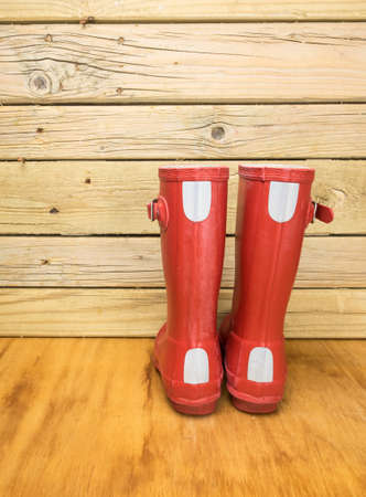rear view of a childs red rubber boots against an aged wooden boardsの写真素材