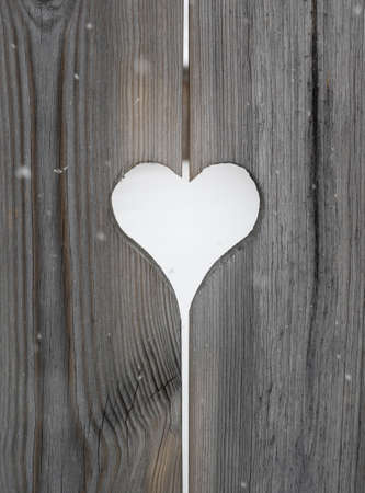 heart motif in grey aged wooden shutterboard fence with  with tree and heart motifs  out of focus in fence behind and falling snowfalkes out of focus in forgroundの写真素材