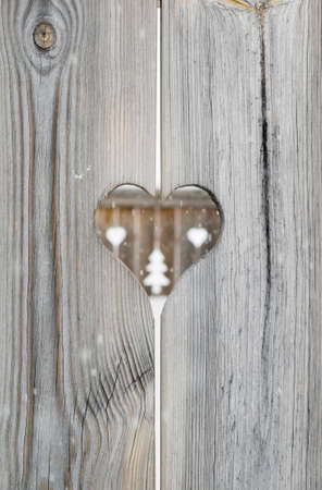 heart motif in grey aged wooden shutterboard fence with  with tree and heart motifs  out of focus in fence behind and falling snowfalkes out of focus in forgroundの写真素材