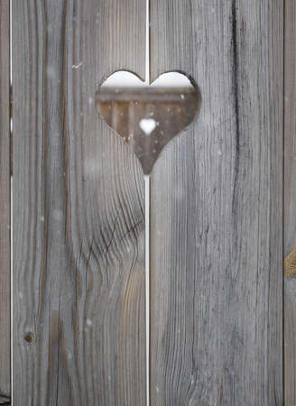 heart motif in grey aged wooden shutterboard fence with  with heart motif  out of focus in fence behind and falling snowfalkesの写真素材