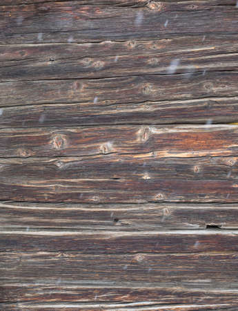 knotted aged dark wooden cabin wall with falling snow with movement blur in foregroundの写真素材